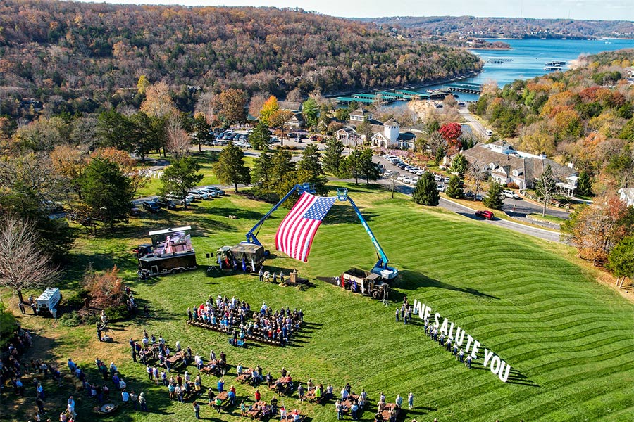 Large American Flag Suspended in the air with a crowd saluting it.