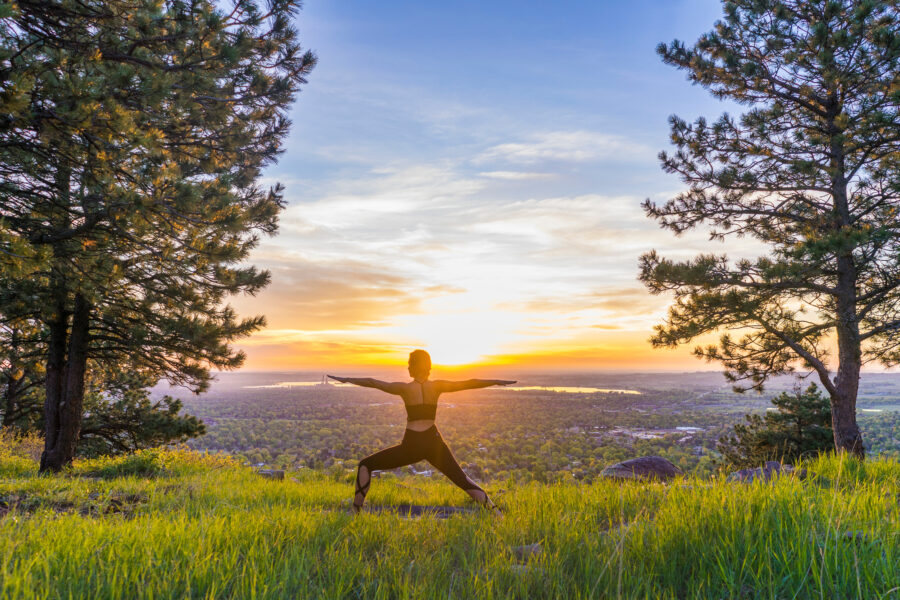 Girl does yoga at sunrise on grassy hill between two trees. Yoga on the summit at sunrise